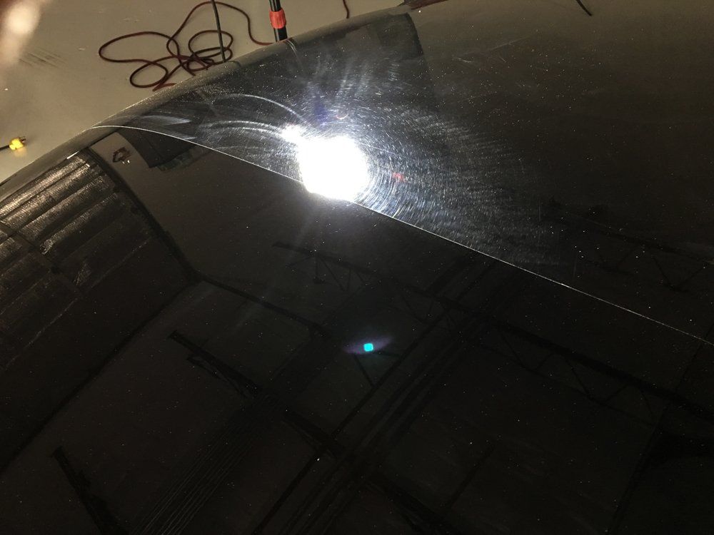 Black car hood with scratches reflecting a bright light.