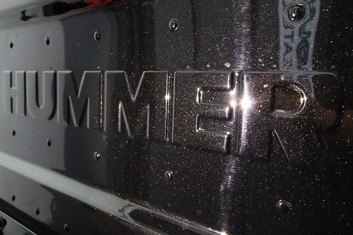 Close-up of black Hummer logo with rivet details and shimmering paint.