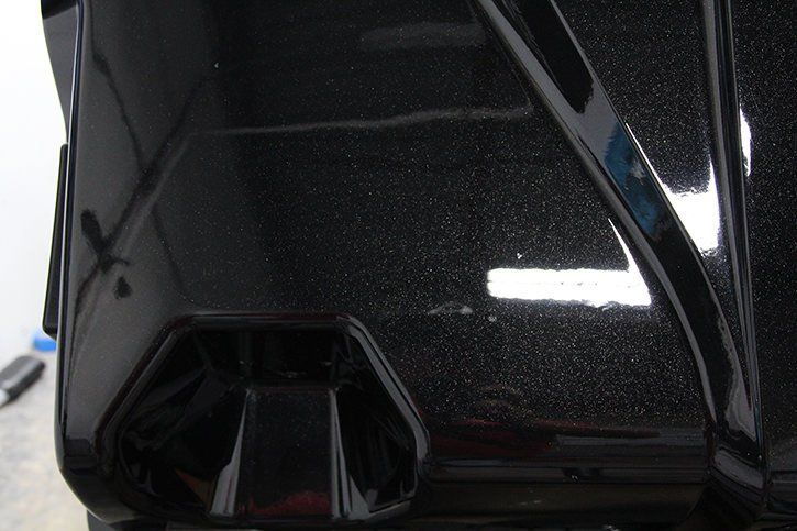 Close-up of black vehicle body with reflective, speckled paint, highlighting surface details.