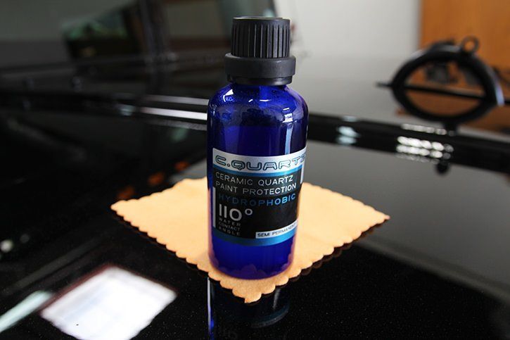 Blue bottle of car paint protection on a microfiber cloth on a black car.