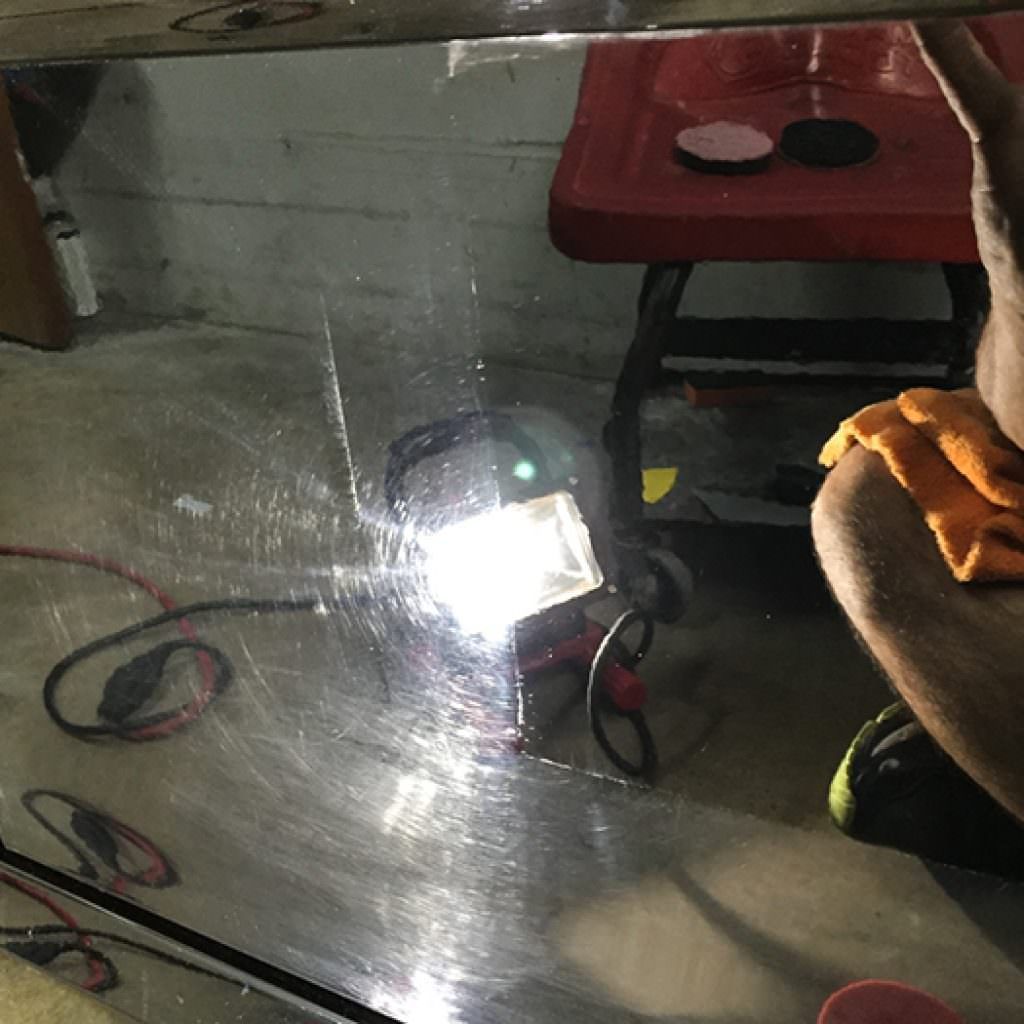 Person polishing a car surface with a light illuminating swirls and scratches.