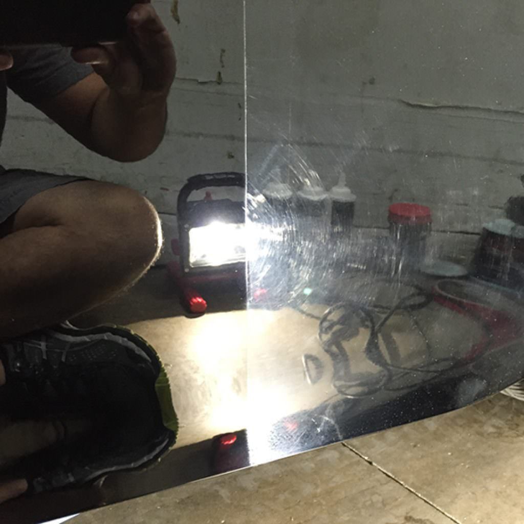 Person polishing black car, revealing clear paint on the left; the right side shows scratched paint.