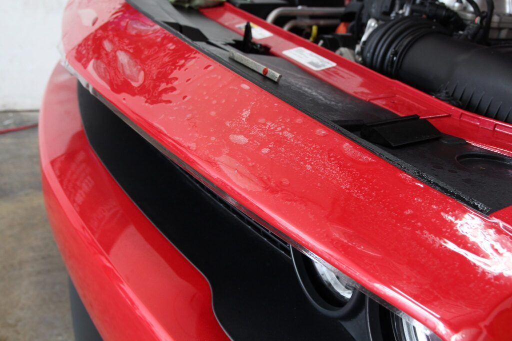 Red car front with wet surface and black trim.