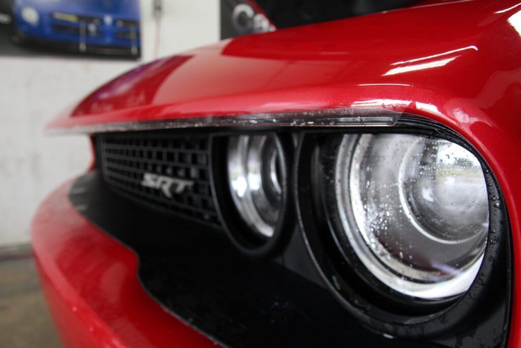 Red Dodge Challenger's close-up view. Grille, SRT emblem, and headlights are visible.