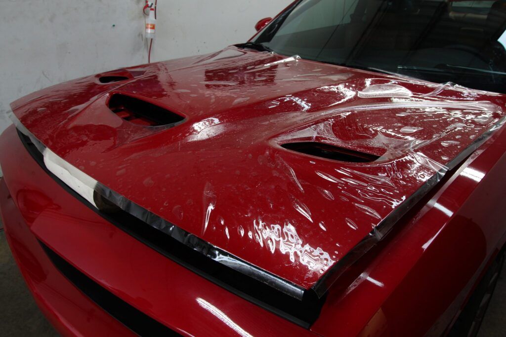 Red car hood covered in plastic wrap, likely for paint protection.