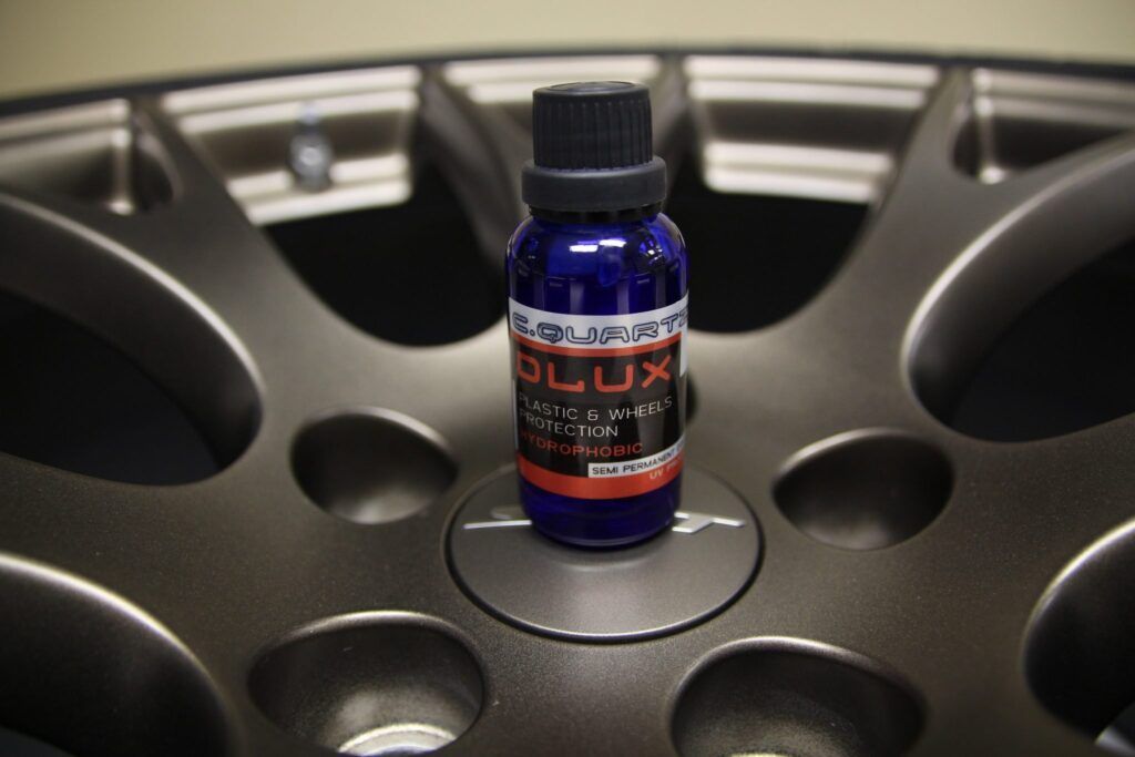 A bottle of car sealant sits on a dark-colored wheel's center hub.