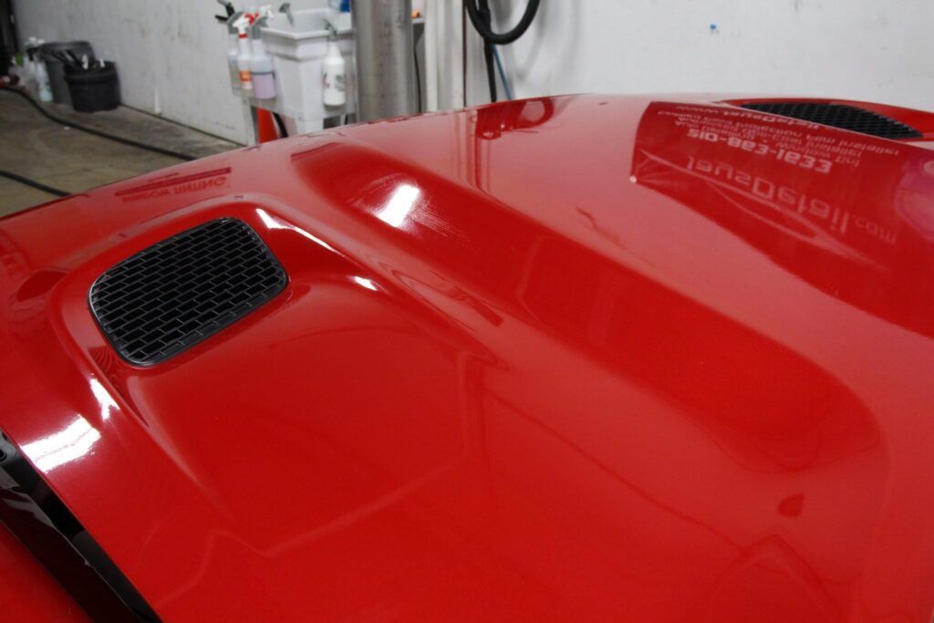 Red car hood with a black vent reflecting the overhead lights and a business name.