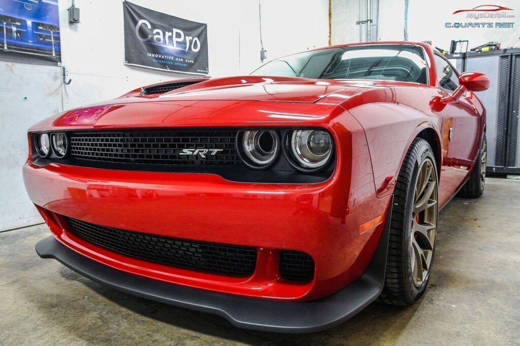 Red Dodge Challenger sports car in a garage, with a black front splitter.