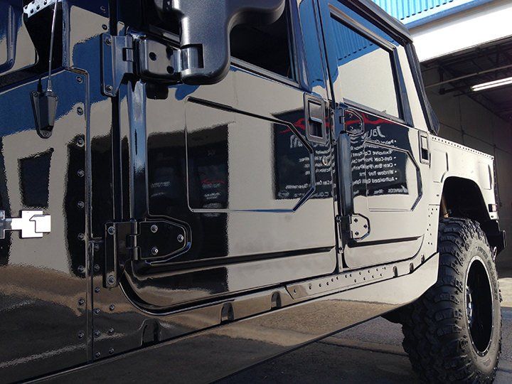 Black Hummer H1 with shiny, clean exterior parked outside. Reflections in the paint show the setting.