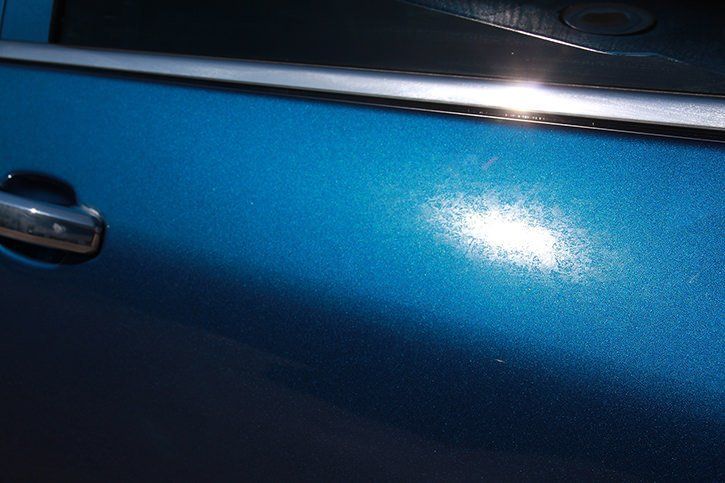 Blue car door with a bright sunlight reflection and chrome trim.