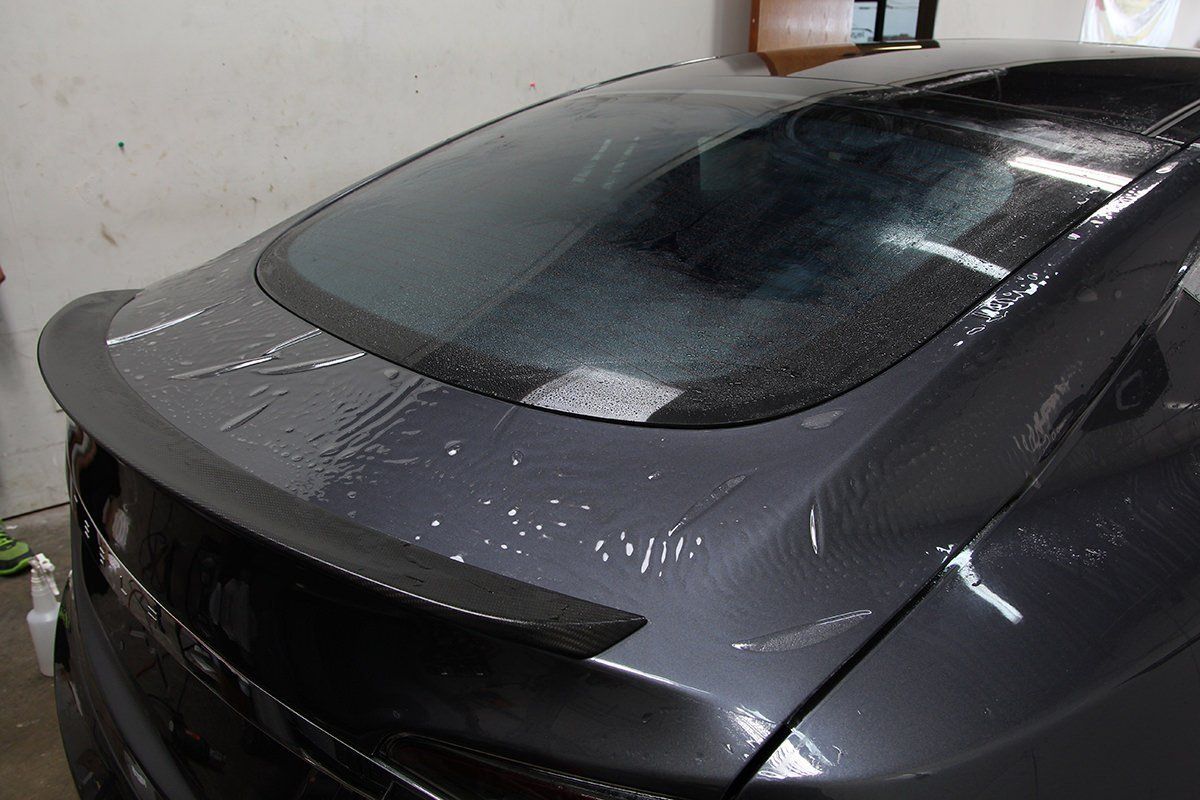 Dark gray car's rear, a spoiler and wet surfaces, in a shop setting.