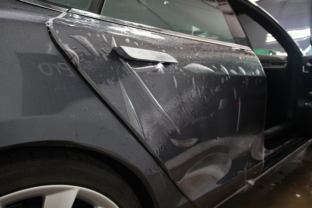 Car door covered in clear protective film, showing installation process.
