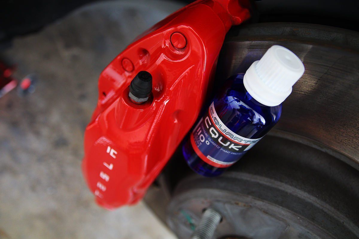 Red car brake caliper with a blue bottle of spray cleaner next to a brake disc.