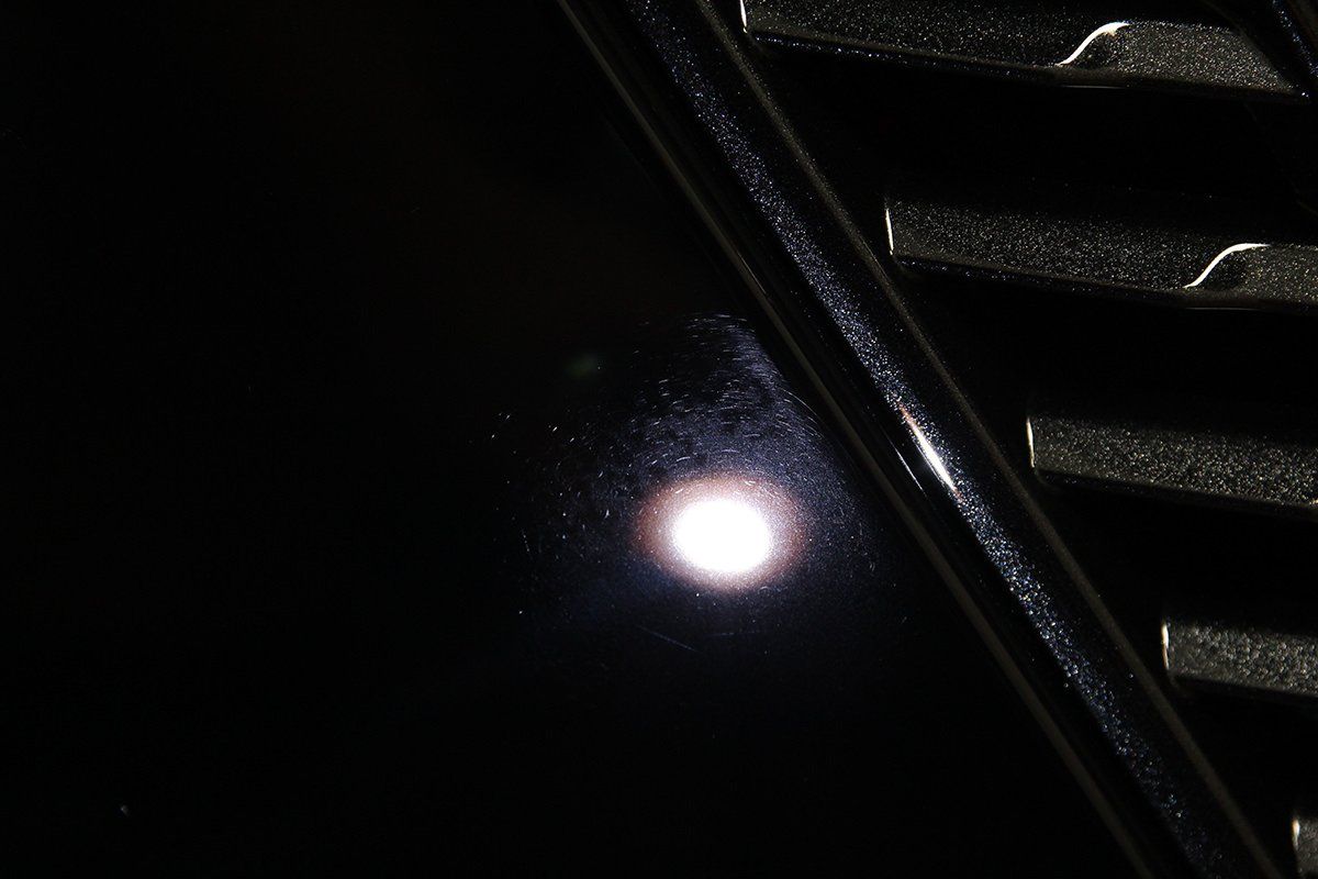 Shiny black car panel with a bright reflection and chrome grill.