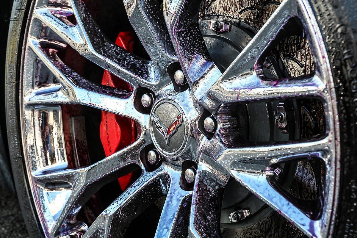 Close-up of a shiny chrome car wheel with a red brake caliper, Corvette logo on the hub.