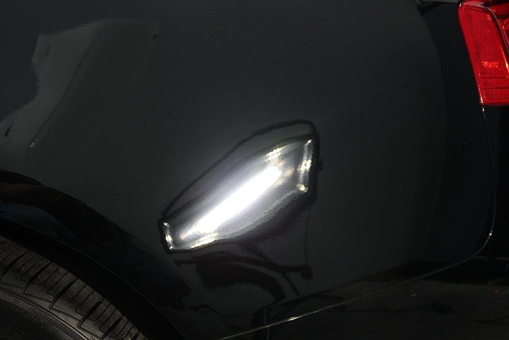 Black car body with a dent reflecting bright light.