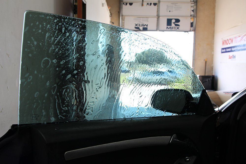 Car window being tinted, with water and film applied. Shop interior with open garage door.