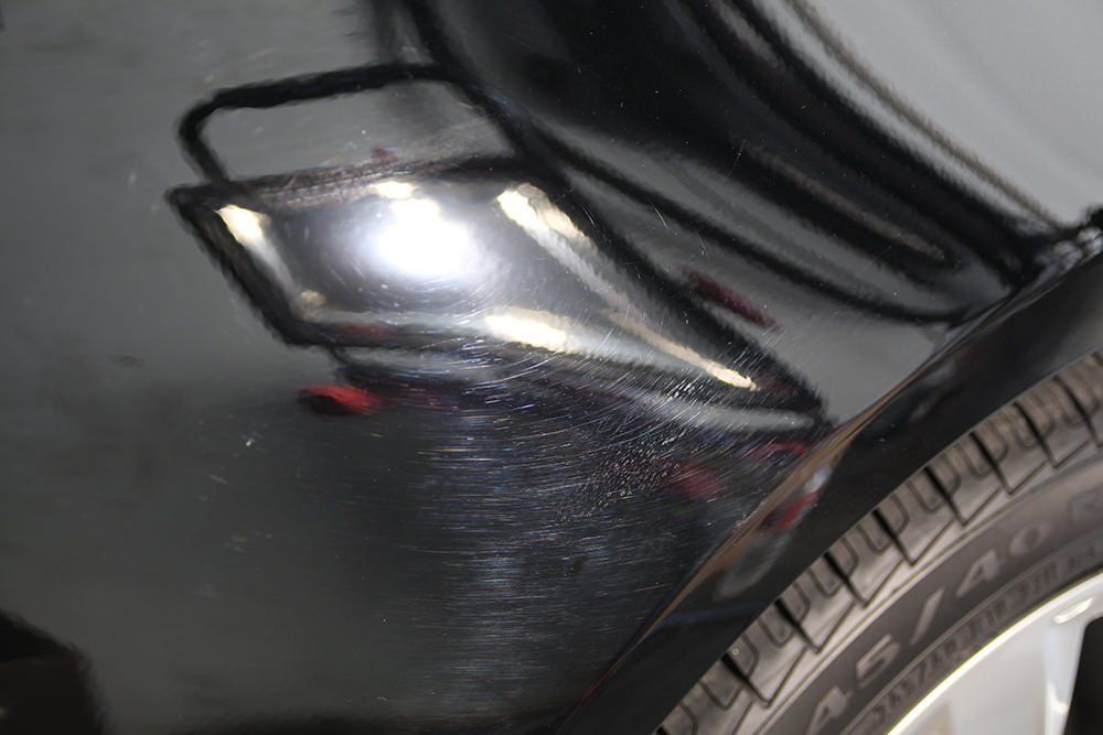 Black car with scratches and a dent on the side, near a tire.