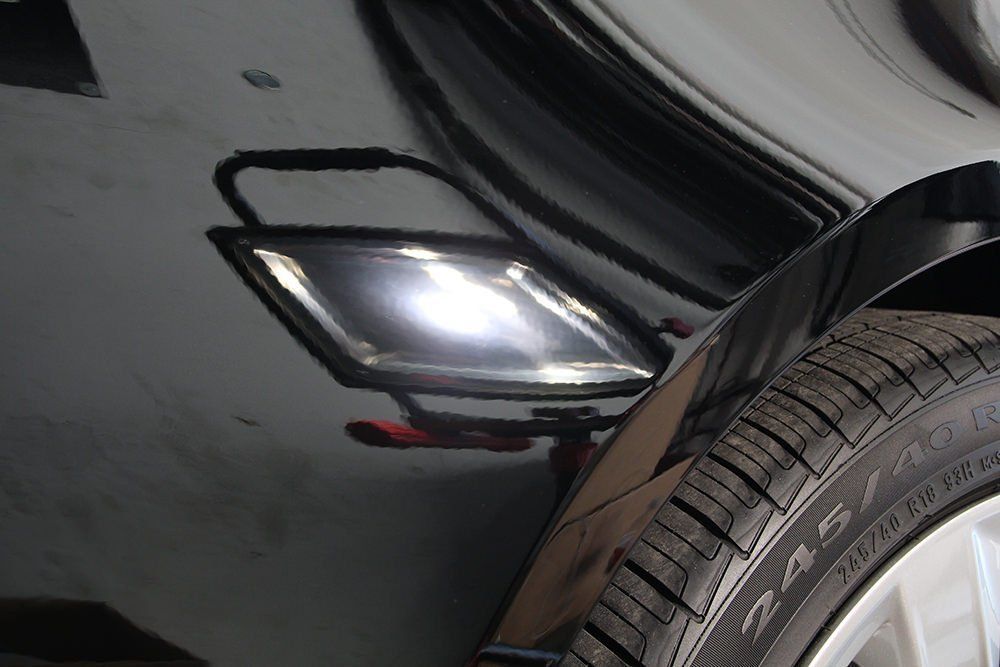 Black car with tire, side marker light reflection on body.