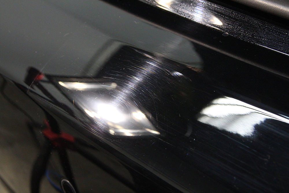 Black car paint surface with visible swirl marks and scratches reflecting light.