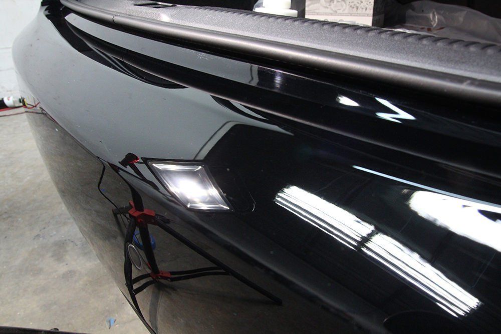 Close-up of a shiny black car bumper with a white rectangular light illuminated.