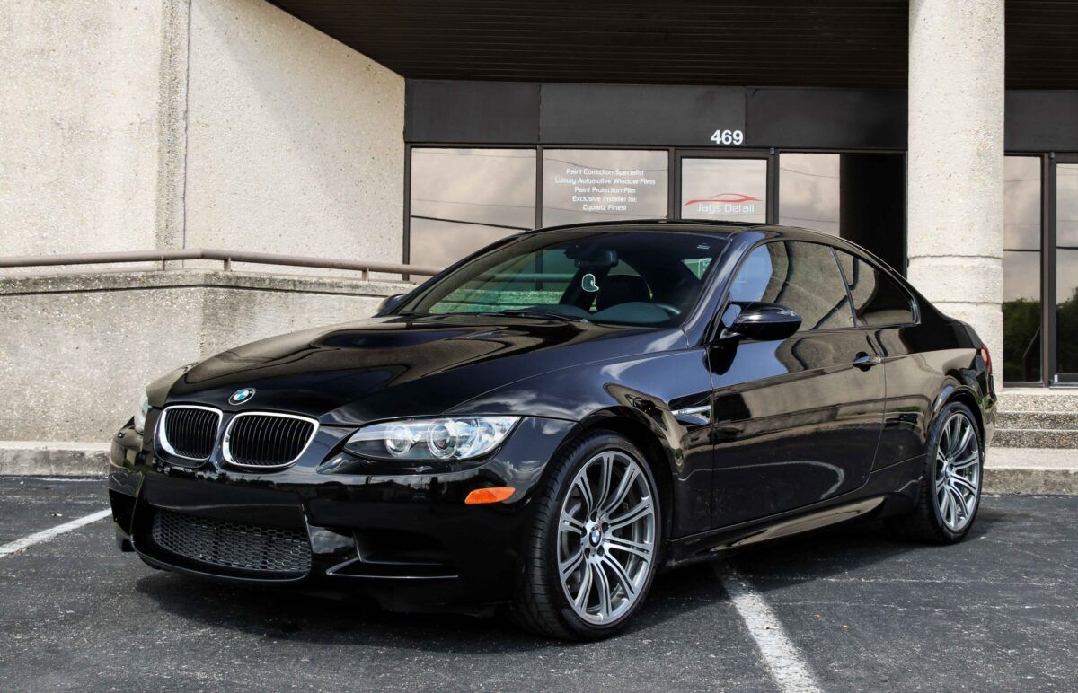 Black BMW M3 coupe parked outside a building with a gray facade.