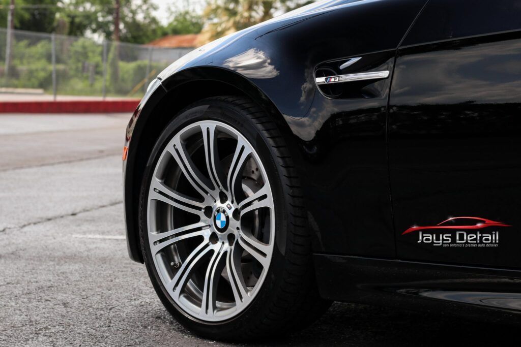 Black BMW car wheel close-up with silver and black rims, parked outside.