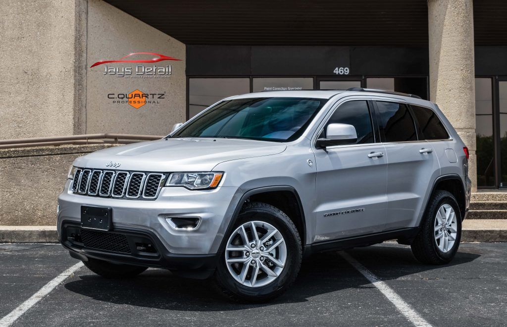Silver Jeep Grand Cherokee parked in front of a building with a sign, under a sunny sky.