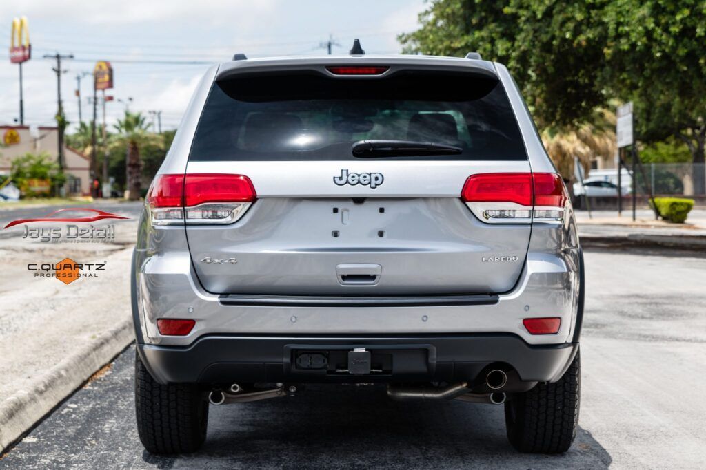 Silver Jeep Grand Cherokee from the rear. Tail lights are red. Parked on a street.
