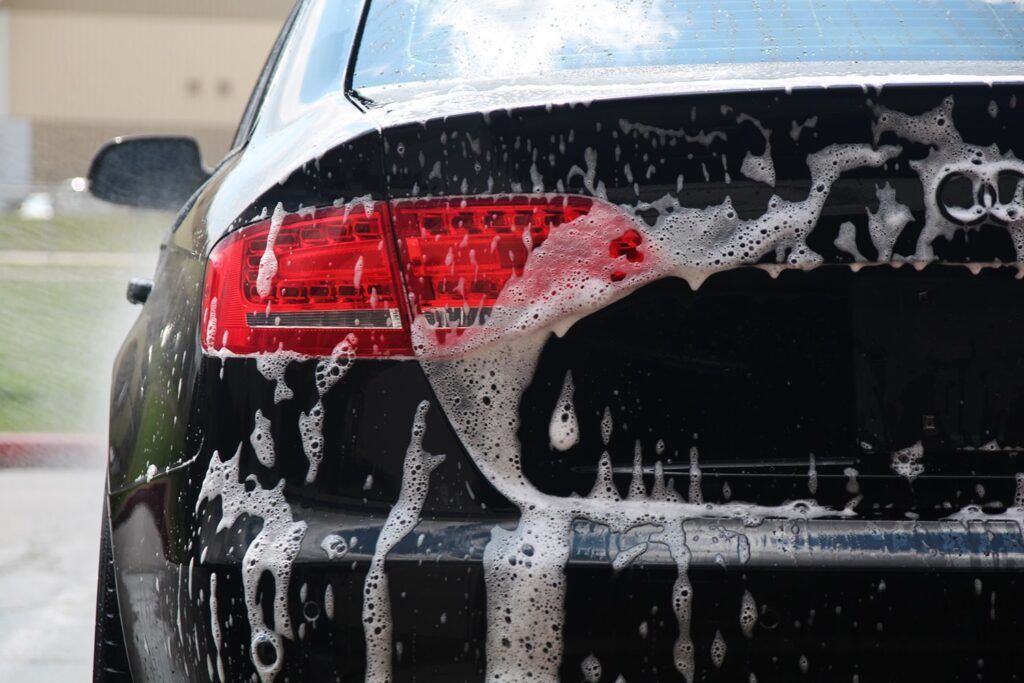 Black car being washed, covered in soapy foam and water.