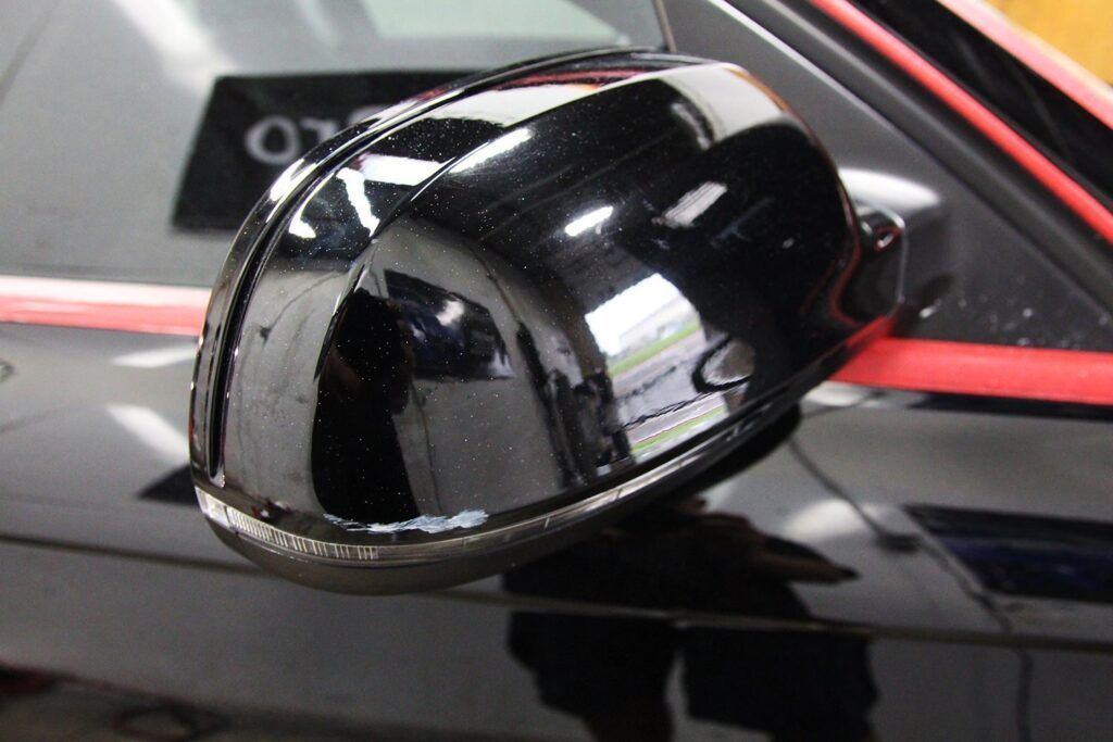Black car side mirror, glossy finish, reflecting the environment, mounted on a black car.