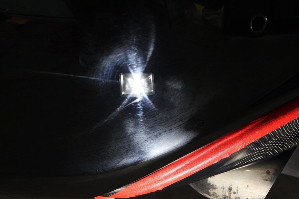Black car surface with bright light shining on a metal fixture, red strap in the bottom right.