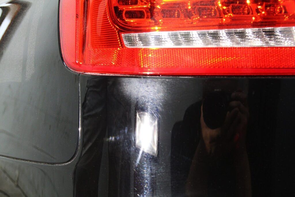 Close-up of a black car's rear bumper, showing a red tail light and a vertical scratch.