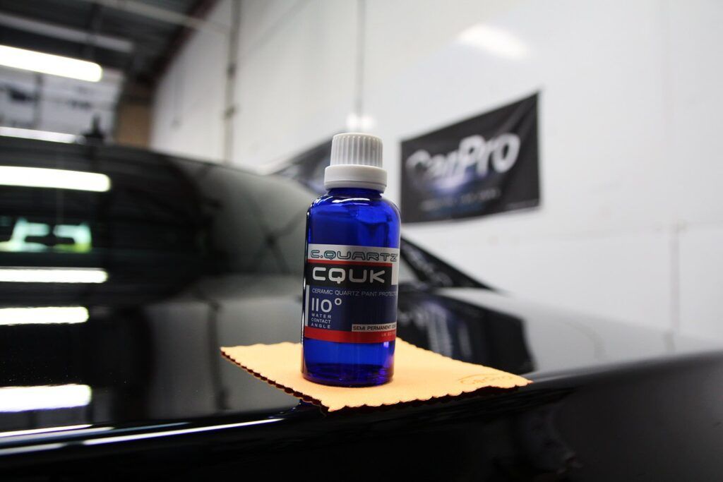 Blue bottle of car detailing product on a microfiber cloth, in front of a black car, in a shop.