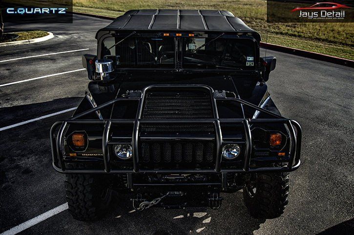 Black Hummer with heavy-duty front grill and bumper. Parked on asphalt with street lines.