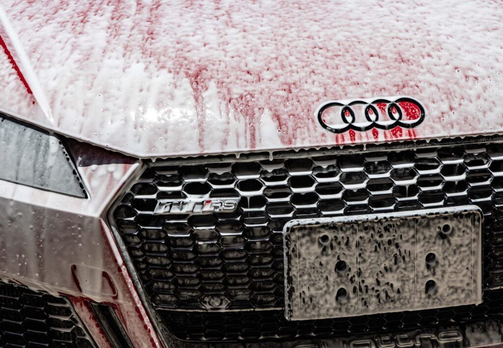 Red Audi car covered in foam during a wash, with the Audi logo visible.