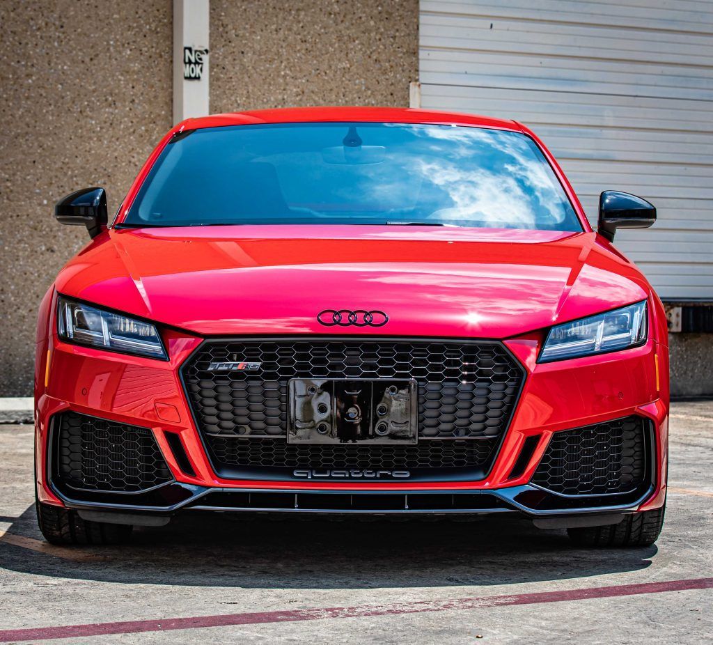 Red Audi TT RS parked in front of a building with a black grill and black accents.