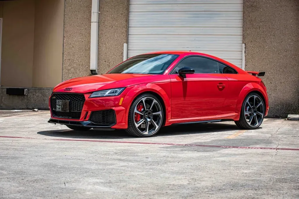 Red Audi TT RS coupe parked in front of a building with a gray garage door.