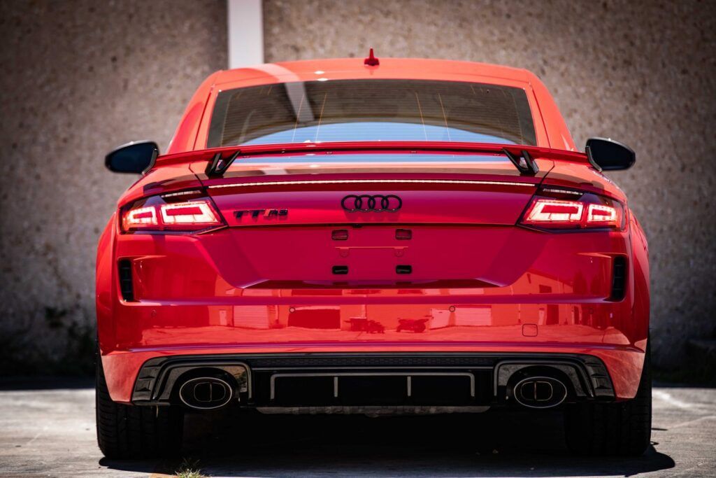 Red Audi TT RS from the rear, parked near a beige wall.