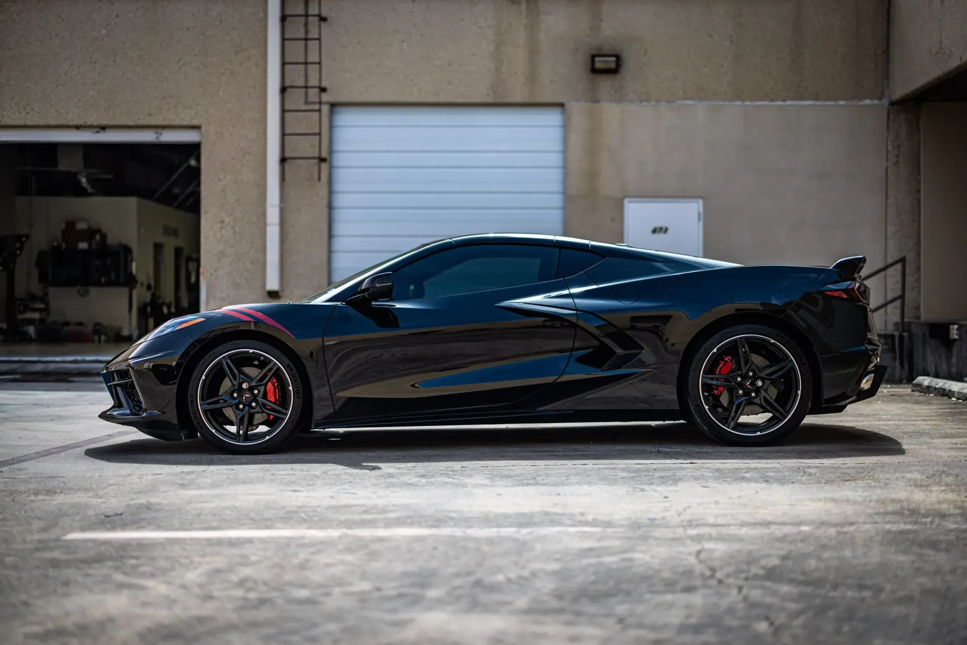 Black sports car parked outside a building, with red brake calipers and custom wheels.