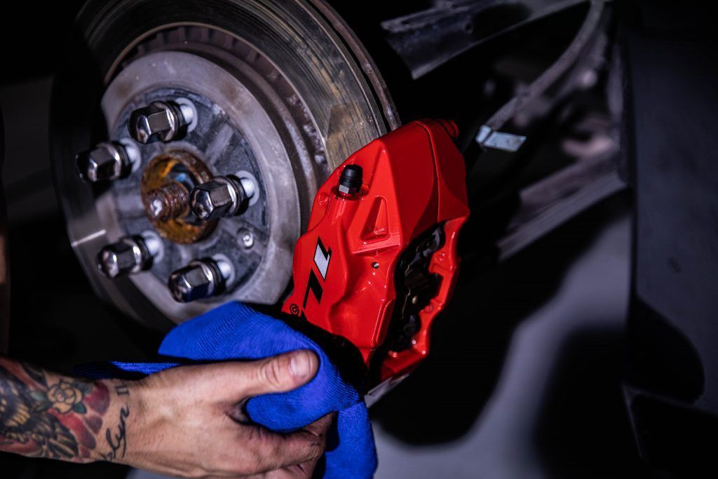 Person cleaning a red brake caliper on a car. The setting is a garage or repair shop.