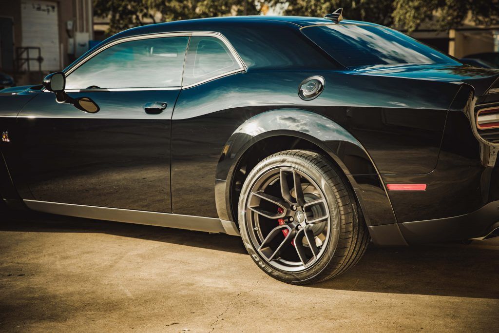 Black Dodge Challenger, parked on a cement surface, with dark tinted windows and chrome rims.