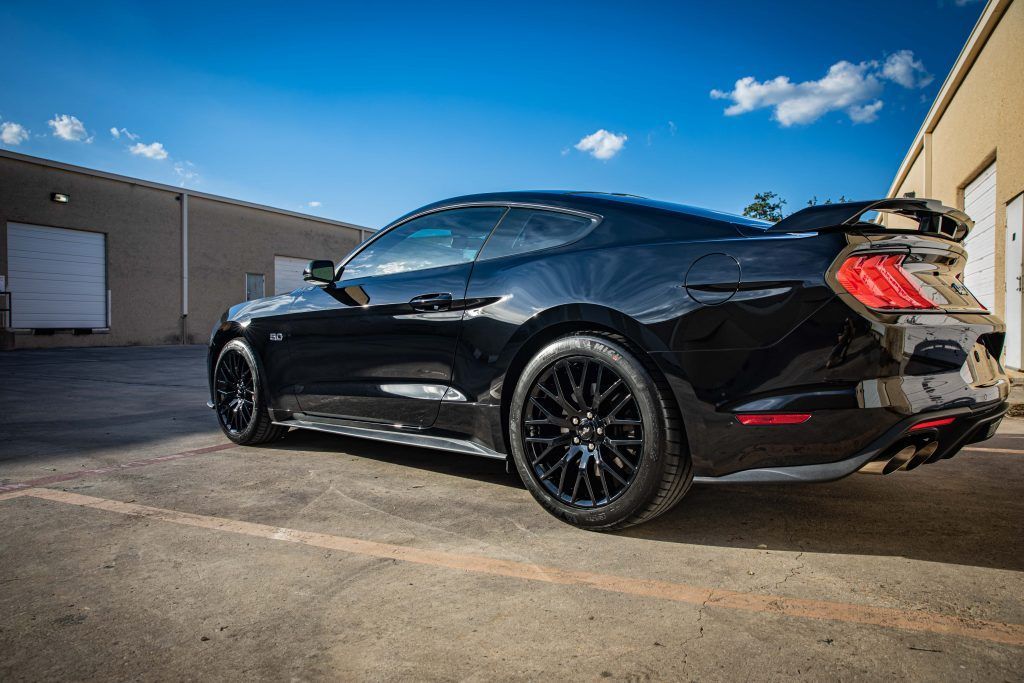 Black Ford Mustang parked outside under a blue sky.