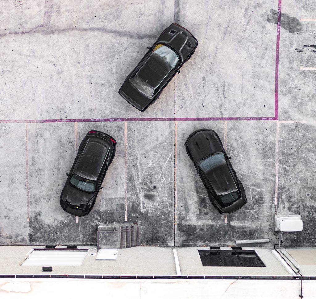 Three black toy cars on a concrete surface. One angled at the top, two at the bottom.