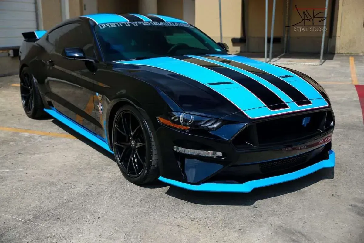 Black Ford Mustang with turquoise racing stripes, trim, and spoiler parked outdoors.