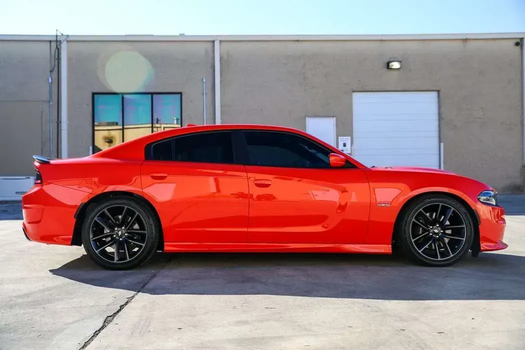 Bright orange Dodge Charger, black rims, parked outside a building.