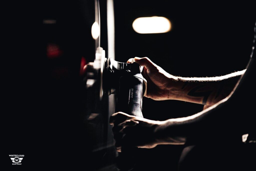 Hands holding a camera in a dim setting; a tattoo is visible on one arm.