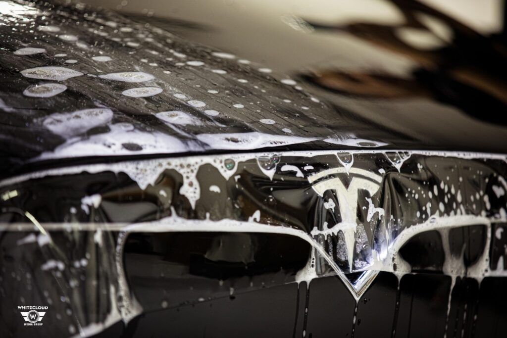 Tesla emblem covered in soapy film during paint protection film installation.