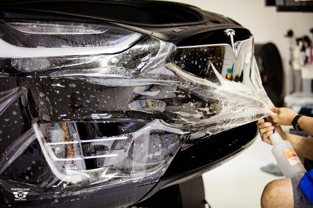 Person applying protective film to a black Tesla front.