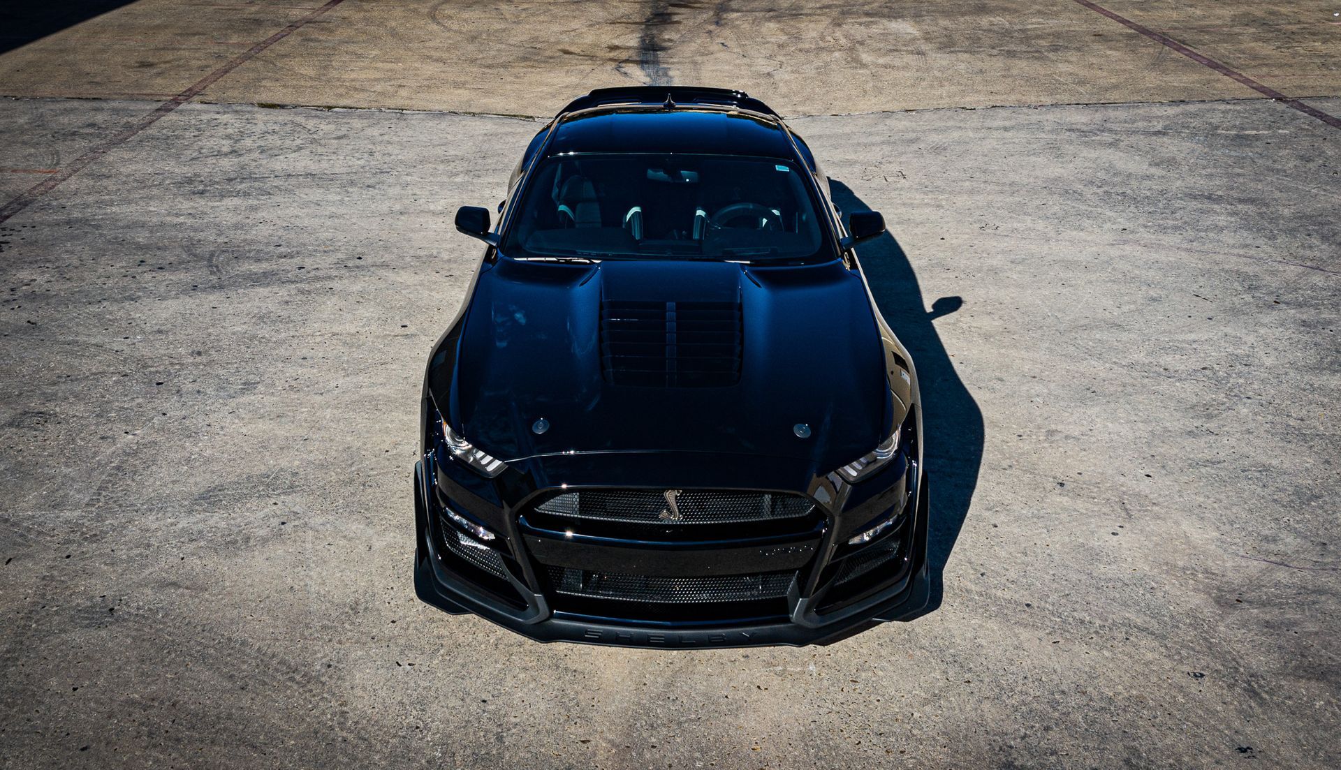 Black Ford Mustang Shelby GT500 parked on concrete, front view, in sunlight.